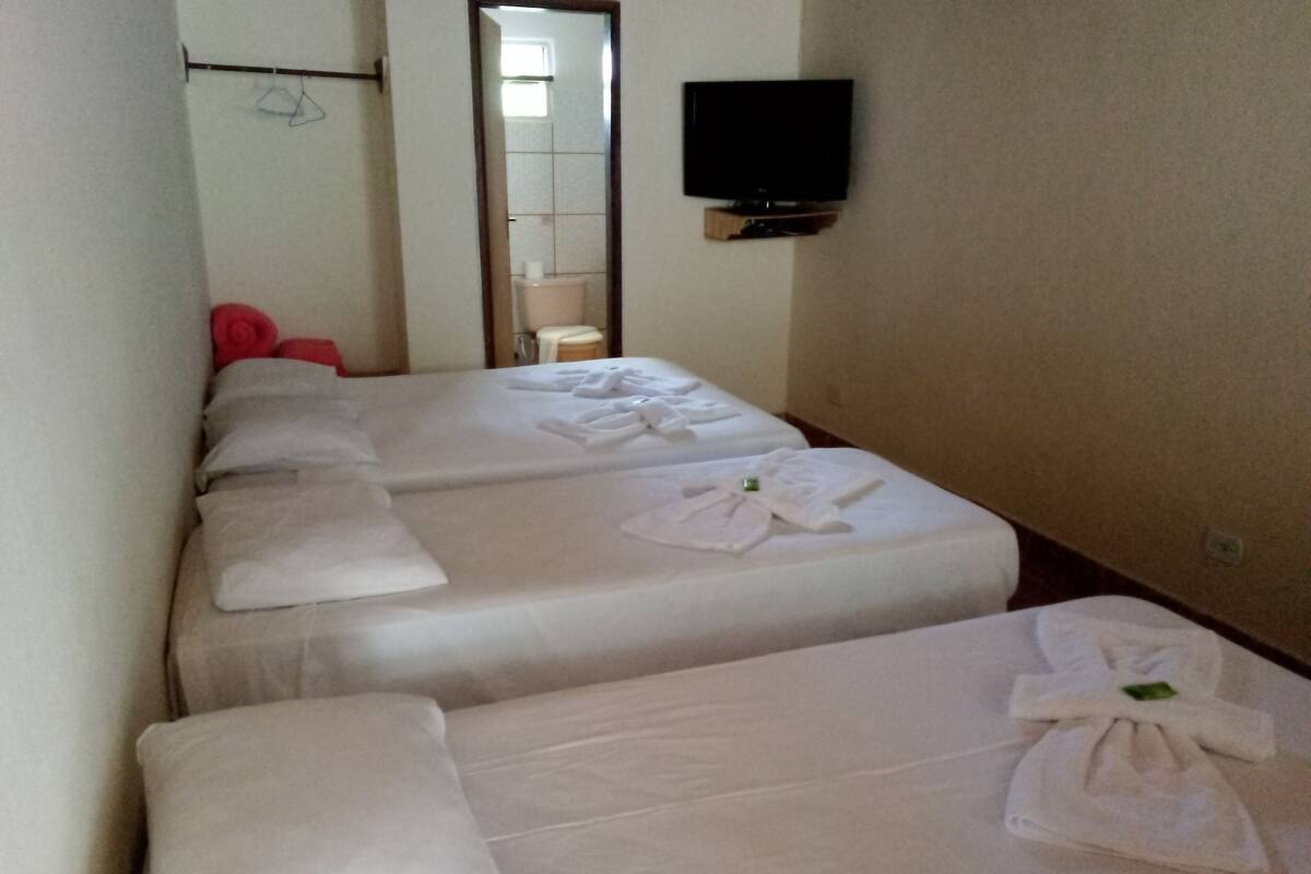 A hotel room with two beds, each with neatly folded towels and pillows. A flat-screen TV is mounted on the wall above the beds.