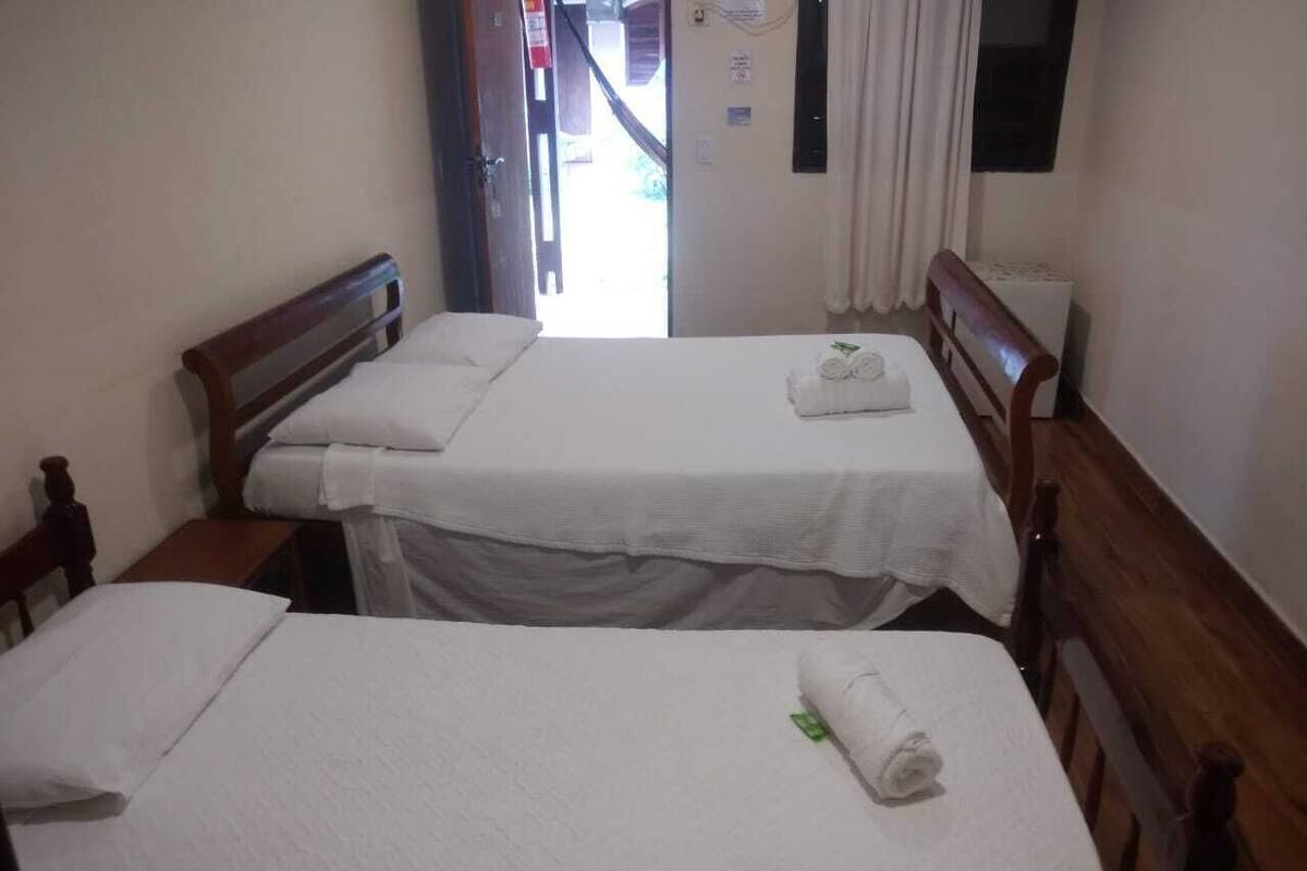 A hotel room with two single beds, a wooden headboard, a small table, and a window with curtains.