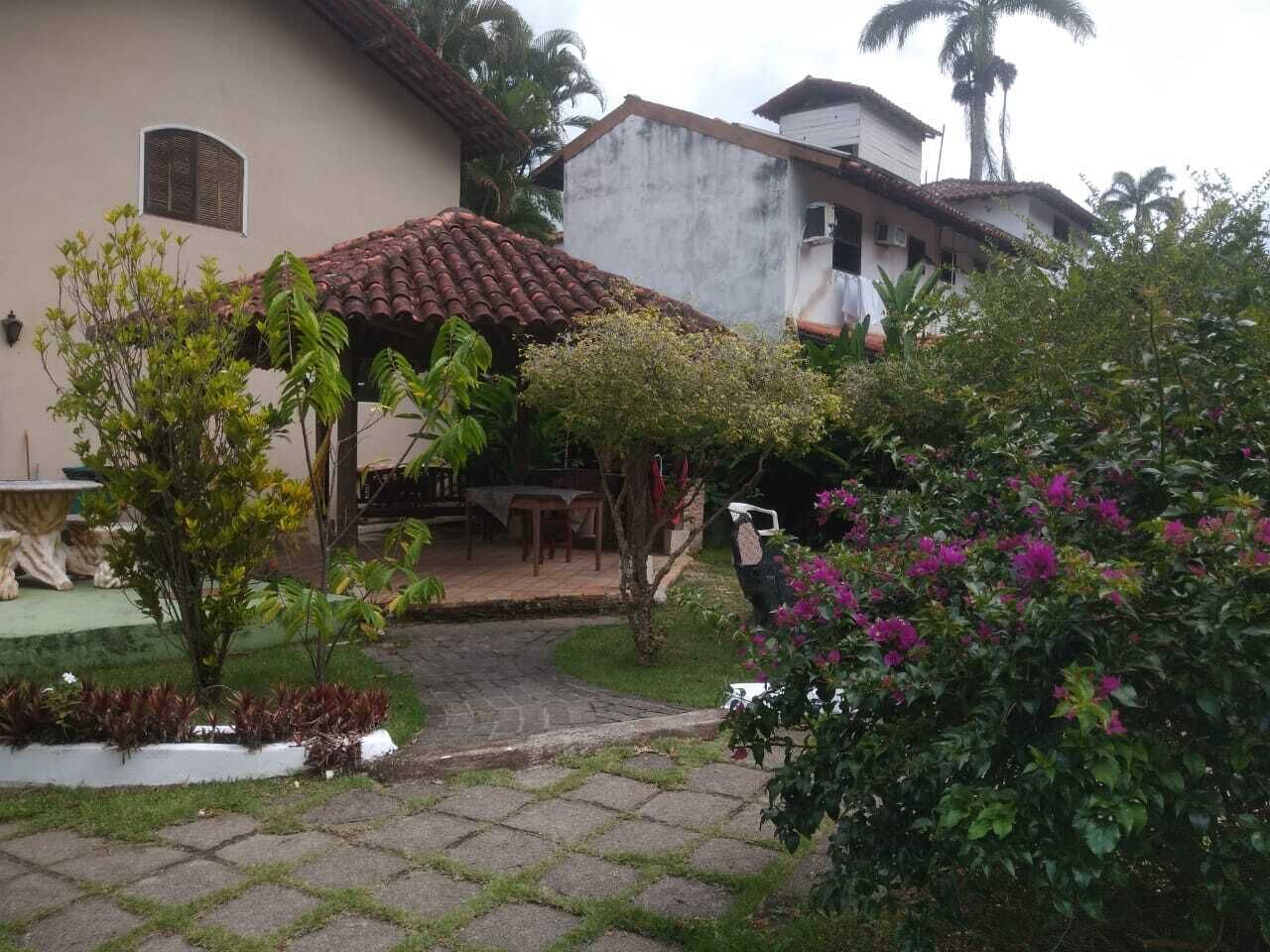 Un patio con suelo de baldosas, una zona de estar techada y una variedad de plantas y flores.