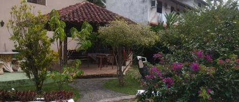 Un patio con suelo de baldosas, una zona de estar techada y una variedad de plantas y flores.