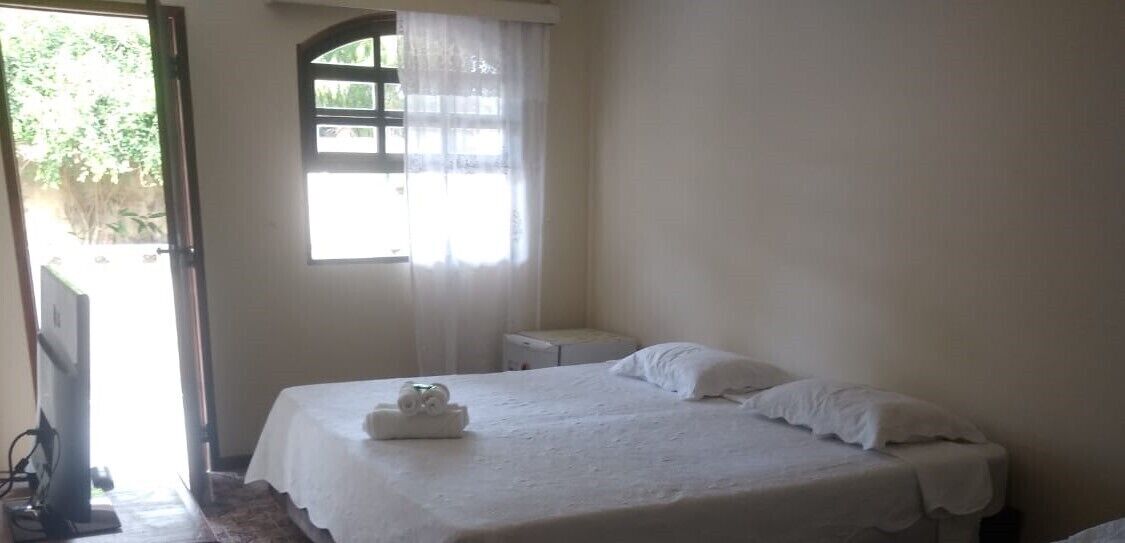 Una habitación sencilla y limpia con una cama, una mesita de noche pequeña y una ventana con cortinas.