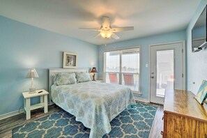 Une chambre à coucher comprenant un lit, une table de chevet, un ventilateur de plafond, une fenêtre avec des stores et une porte.