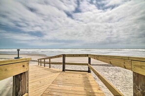 Une promenade en bois mène à une plage de sable, sous un ciel nuageux.