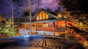 Een houten chalet met een veranda, een trap en uitzicht op de nachthemel.