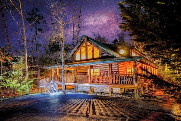 A log cabin with a porch, a staircase, and a view of the night sky.