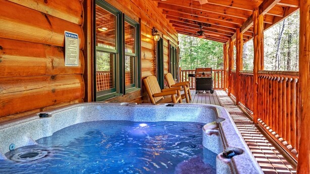 Een houten hut met een jacuzzi, houten terrasstoelen en een barbecue.