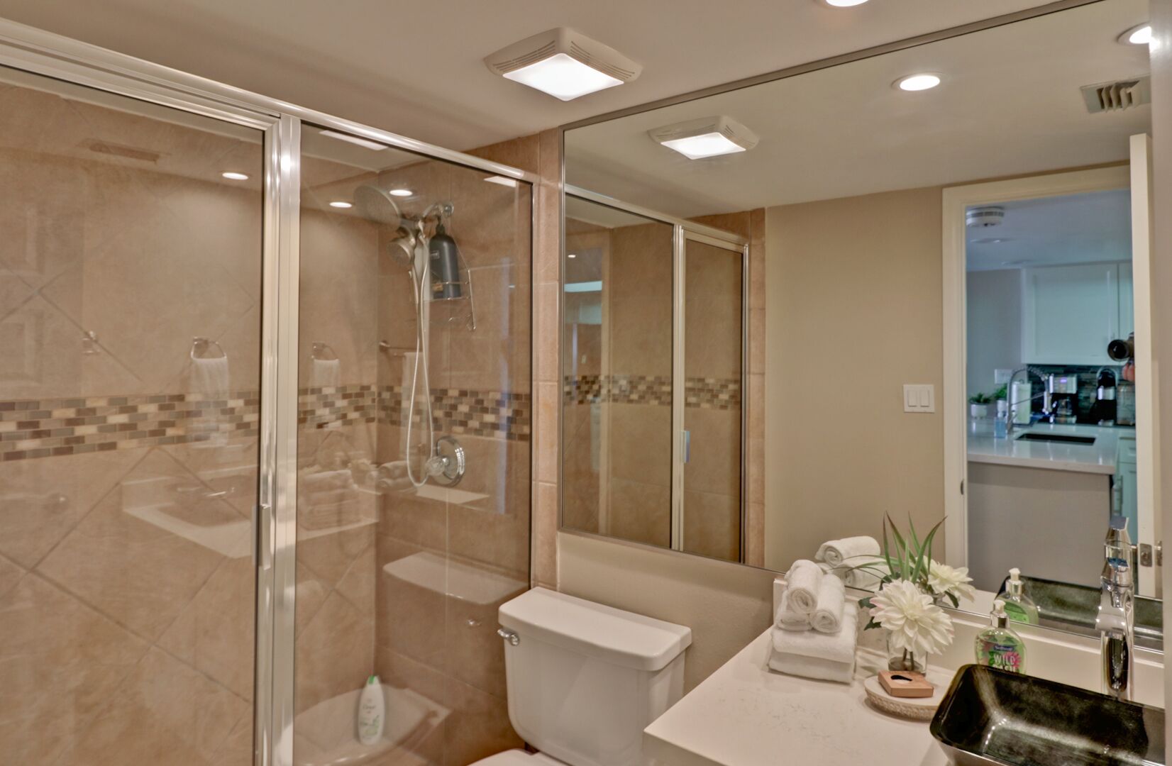 A modern bathroom with a glass-enclosed shower, a toilet, and a sink area with a mirror and toiletries.