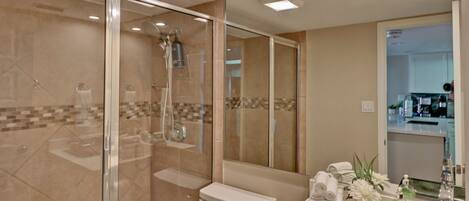 A modern bathroom with a glass-enclosed shower, a toilet, and a sink area with a mirror and toiletries.