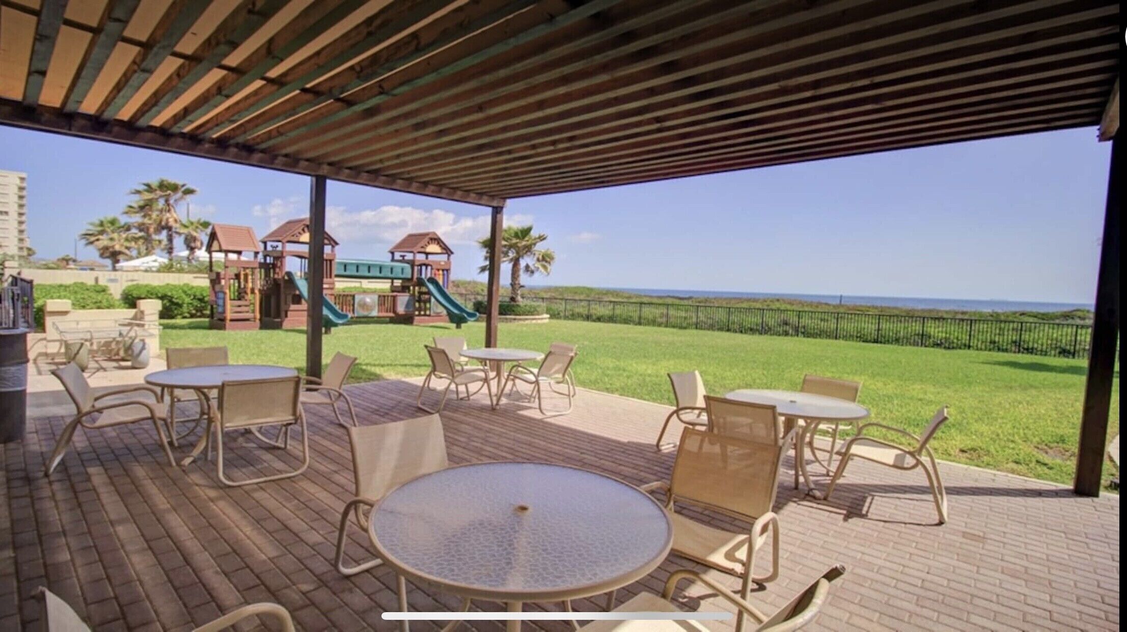 An outdoor patio with tables and chairs, a playground in the background, and a view of the ocean.