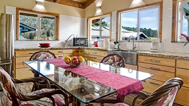Una cocina moderna con armarios de madera, una mesa de comedor de vidrio y grandes ventanales que ofrecen vistas al exterior.
