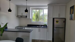 Una cocina moderna con armarios blancos, encimera negra, refrigerador de acero inoxidable y ventana con vistas a la vegetación.