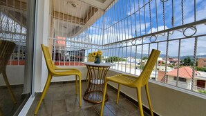 Un balcón con sillas amarillas, una mesa pequeña y vistas de la ciudad.