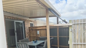 A covered patio area with a table and chairs, a wooden fence, and a gravel path. - Jack's Shack - Burrum Heads - Relax, fish and swim (Burrum Heads)