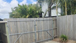 A backyard with a wooden fence, concrete patio, and a small garden area. - Jack's Shack - Burrum Heads - Relax, fish and swim (Burrum Heads)