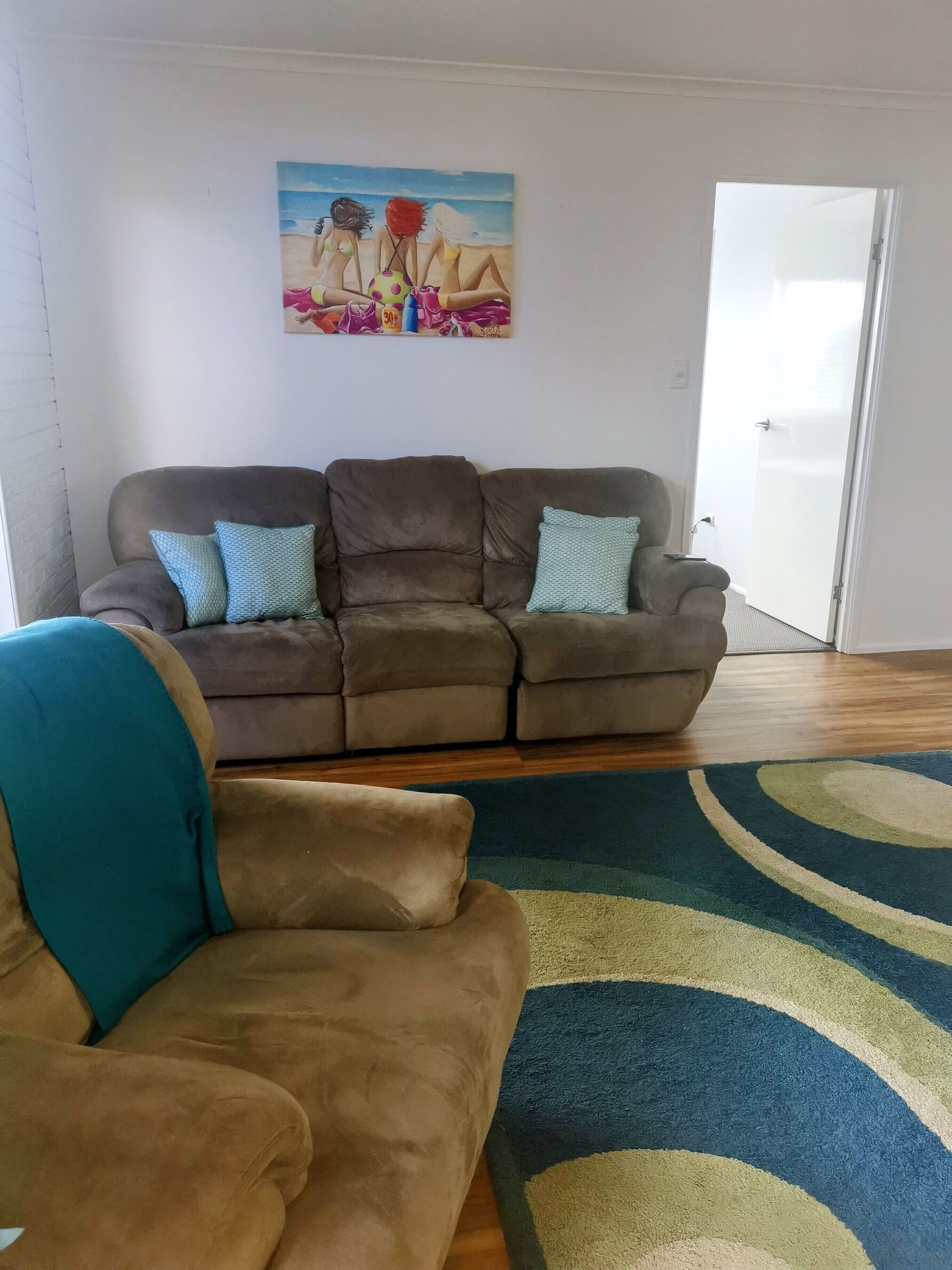 Een woonkamer met een bruine zithoek, een blauwgroene fauteuil en een kleurrijk vloerkleed.