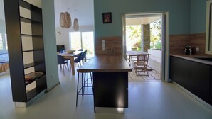 Una cocina moderna con una isla central, un comedor con sillas y una estantería.