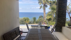 Un patio al aire libre con una mesa y bancos de madera, un pilar de piedra y vista al océano.