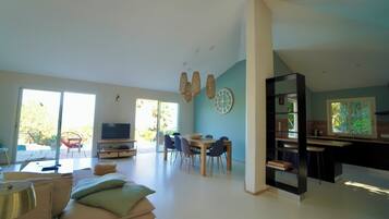 Un grand espace de vie comprenant un coin repas avec une table et des chaises, un téléviseur et un coin cuisine avec un bar.