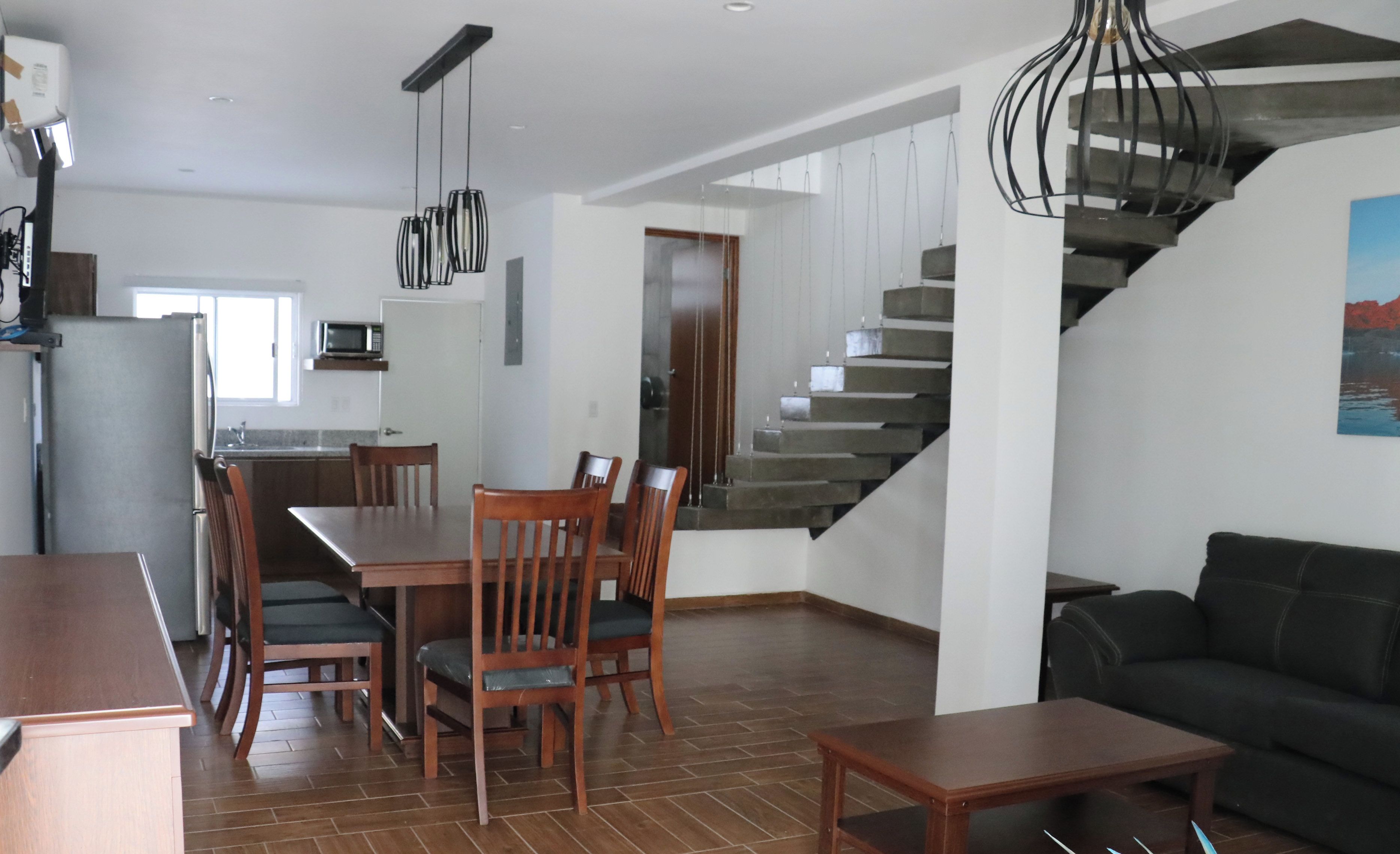 A modern living space with a dining area, kitchen, and staircase.