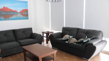 A living room with two black sofas, a wooden coffee table, and a small side table. A painting of a coastal scene is on the wall.