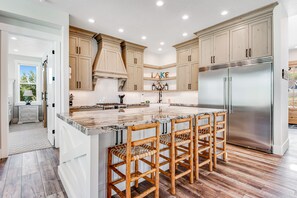 Una cocina moderna con armarios de madera, un refrigerador de acero inoxidable y una isla de mármol con taburetes de bar.
