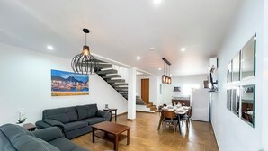 Ett modernt vardagsrum med en soffa, ett soffbord och en matplats med stolar och ett bord. En trappa leder upp till ett annat plan.