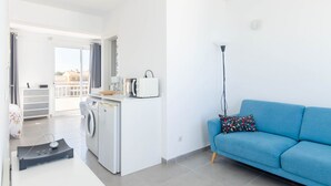 A modern apartment with a kitchen, a blue sofa, a washing machine, and a view to the outside. - YourHouse Monges sea view-studio (Can Picafort)