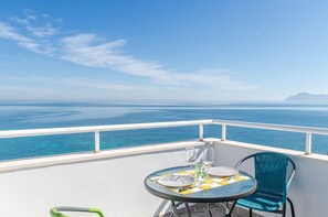En balkon med et bord dækket til to, med udsigt over et stort hav.