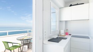 A balcony with a table and chairs, a kitchen area with white cabinets, and a view of the ocean. - YourHouse Monges sea view-studio (Can Picafort)