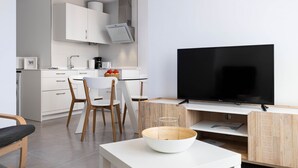 Una cocina moderna con armarios blancos, un comedor con mesa y sillas blancas, y un televisor de pantalla plana montado en un mueble de madera.