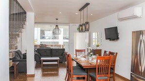 Un salon moderne avec un canapé, une table à manger pour quatre personnes et un coin cuisine visible à travers une cloison en verre.