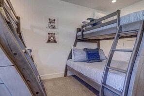 A bunk bed with a ladder, a framed animal picture on the wall, and a door in the background.