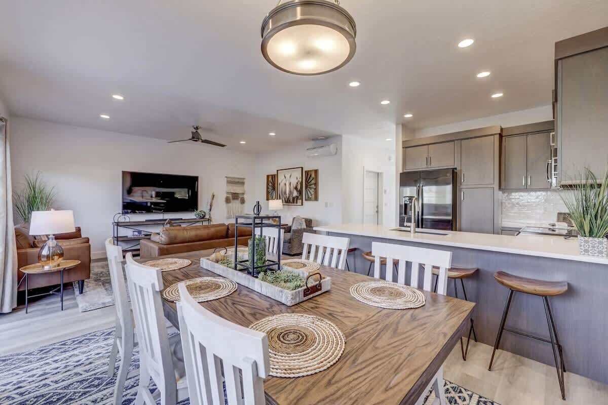A modern kitchen with a central island, white bar stools, and a dining area with a wooden table and white chairs.