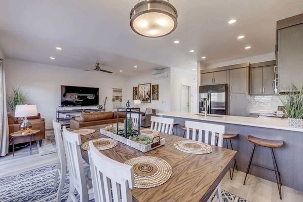 A modern kitchen with a central island, white bar stools, and a dining area with a wooden table and white chairs.