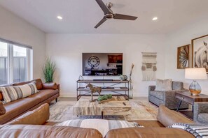A spacious living room with a ceiling fan, a large window, and a view of the kitchen.