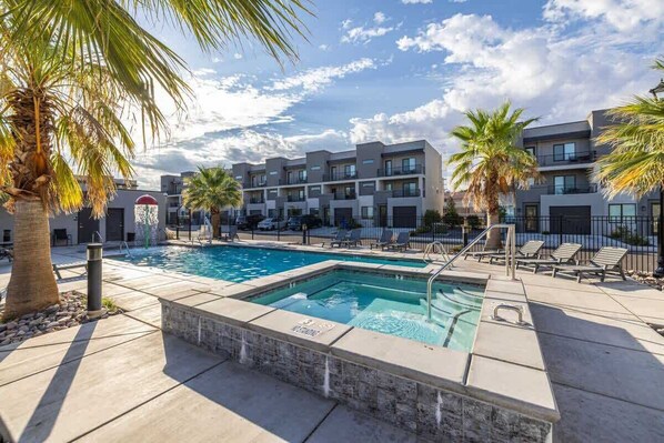 A swimming pool with lounge chairs and palm trees, surrounded by modern apartment buildings.