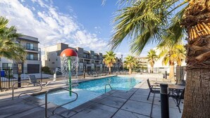 A swimming pool with a water feature, surrounded by palm trees and modern buildings. - The Vue #25 | Luxury Poolside Townhouse (Saint George)