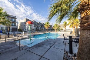 A swimming pool with a water feature, surrounded by palm trees and modern buildings. - The Vue #25 | Luxury Poolside Townhouse (Saint George)
