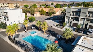 A residential area with a swimming pool surrounded by palm trees and modern buildings. - The Vue #25 | Luxury Poolside Townhouse (Saint George)