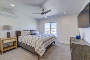 A bedroom with a bed, a nightstand, a desk, a ceiling fan, and a window.