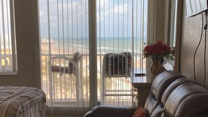 A room with a bed, a leather sofa, a patterned rug, and a view of the beach through large windows. - DAYTONA GETAWAY OCEAN FRONT CONDO (Daytona Beach)
