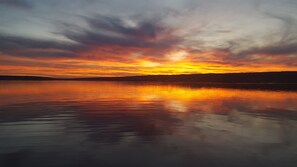 Un coucher de soleil sur une étendue d’eau calme, avec la silhouette d’une terre lointaine à l’horizon.