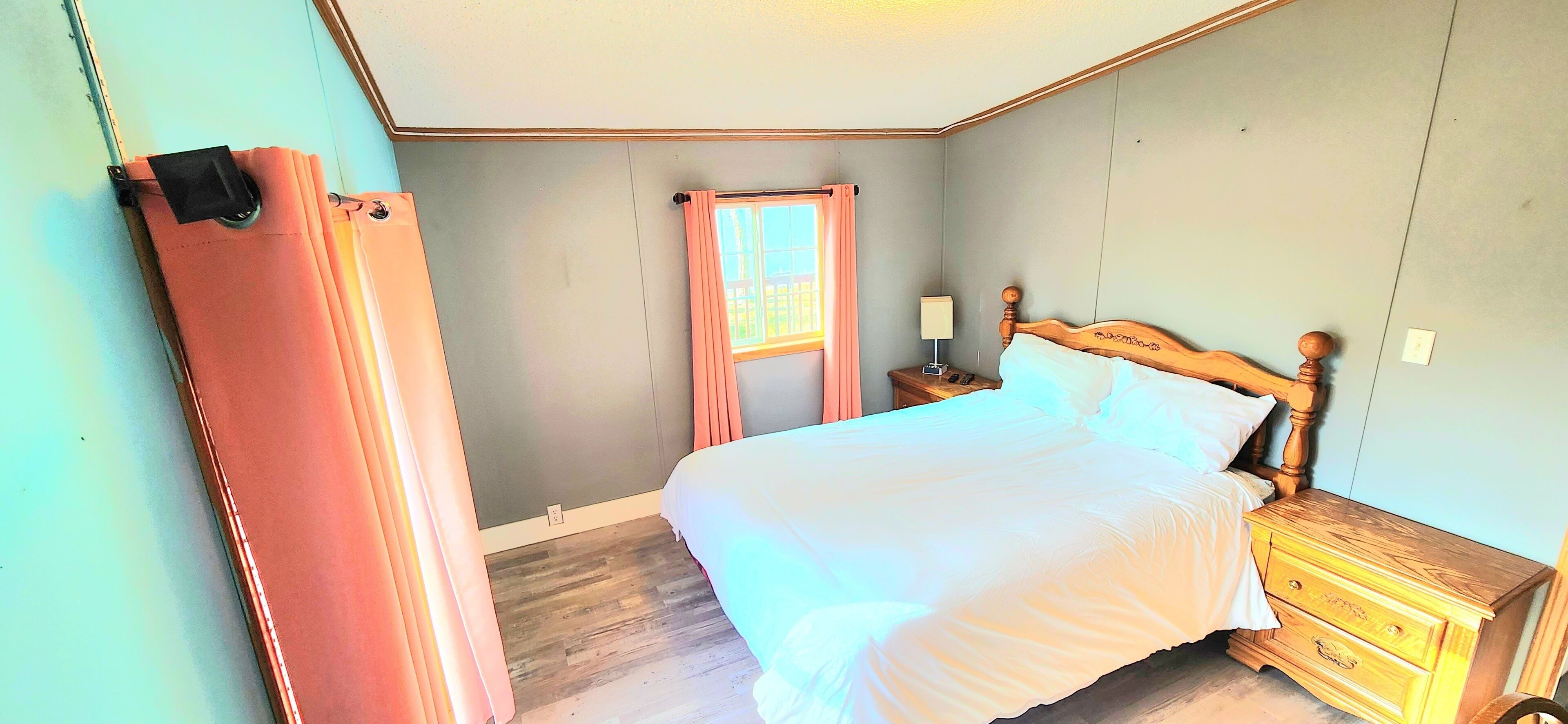 A bedroom with a bed, wooden nightstand, and a window with curtains.