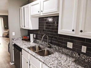 A kitchen with white cabinets, black backsplash, granite countertop, and stainless steel sink.