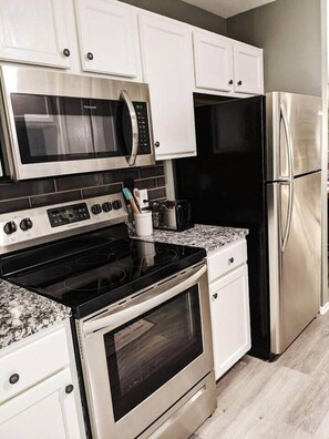 Una cocina moderna con electrodomésticos de acero inoxidable, armarios blancos y encimera de granito.