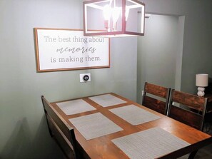 Un comedor con una mesa de madera, cuatro sillas y una cita enmarcada en la pared.