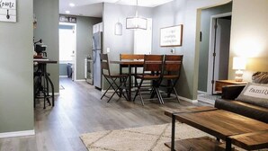 Ett modernt vardagsrum med ett soffbord i trä, en soffa med en kudde med ett ”familjetema” och en matplats med ett bord och stolar i trä.