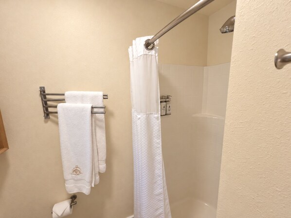 A bathroom with a shower curtain, a towel rack with two towels, and a toilet paper holder.