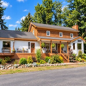A two-story house with a porch, a covered front porch area, and a small front yard with plants and rocks.