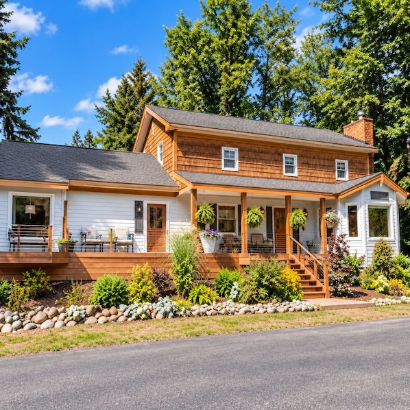 A two-story house with a porch, a covered front porch area, and a small front yard with plants and rocks.